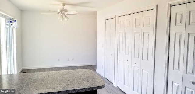 bedroom with ceiling fan, baseboards, two closets, and wood finished floors