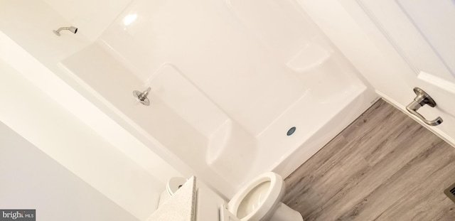 full bath with toilet, a tub to relax in, and wood finished floors