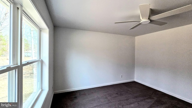 unfurnished room with a ceiling fan, baseboards, and dark colored carpet