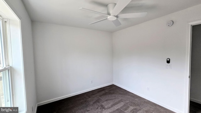 empty room featuring dark carpet, baseboards, and a ceiling fan