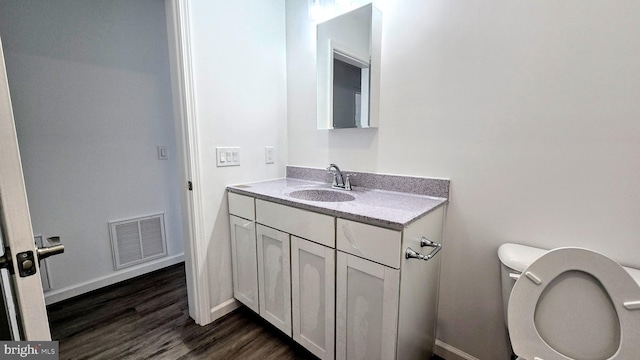 half bath featuring visible vents, baseboards, toilet, wood finished floors, and vanity