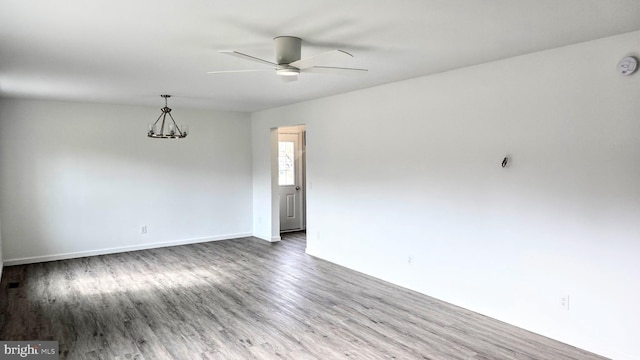 empty room featuring baseboards, wood finished floors, and ceiling fan with notable chandelier