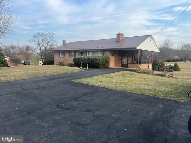 ranch-style house with a front yard, brick siding, driveway, and a chimney