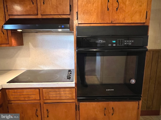 kitchen with black appliances, light countertops, brown cabinets, and under cabinet range hood
