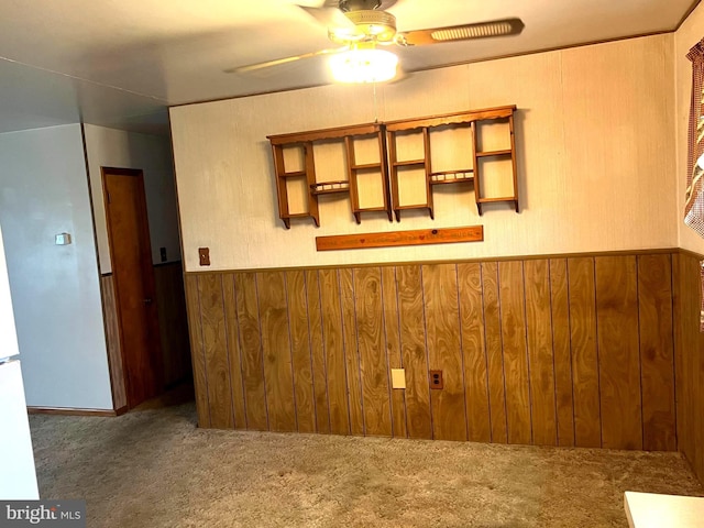 carpeted spare room featuring wooden walls, a ceiling fan, and a wainscoted wall