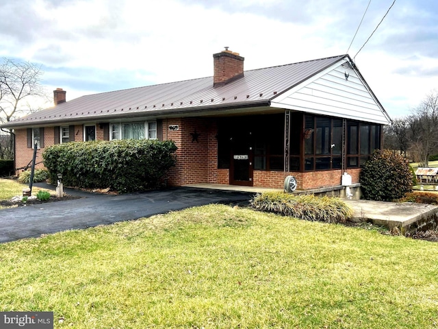 view of front facade with a front lawn, brick siding, a chimney, and a sunroom