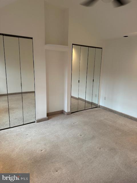 unfurnished bedroom featuring carpet flooring, baseboards, a high ceiling, and multiple closets