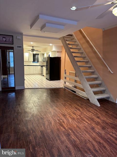 unfurnished living room with visible vents, stairs, a ceiling fan, and wood finished floors