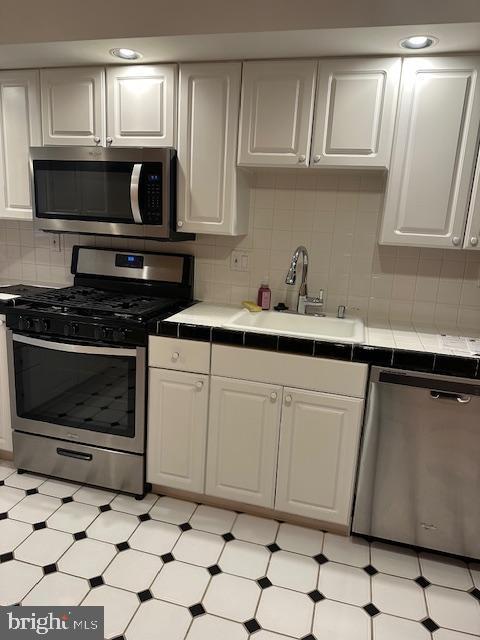 kitchen with a sink, backsplash, appliances with stainless steel finishes, white cabinets, and tile counters