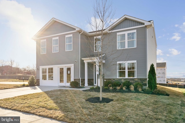 view of front of home with stone siding, concrete driveway, and a front yard