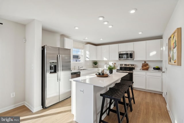 kitchen featuring light wood-type flooring, appliances with stainless steel finishes, white cabinetry, and a kitchen bar