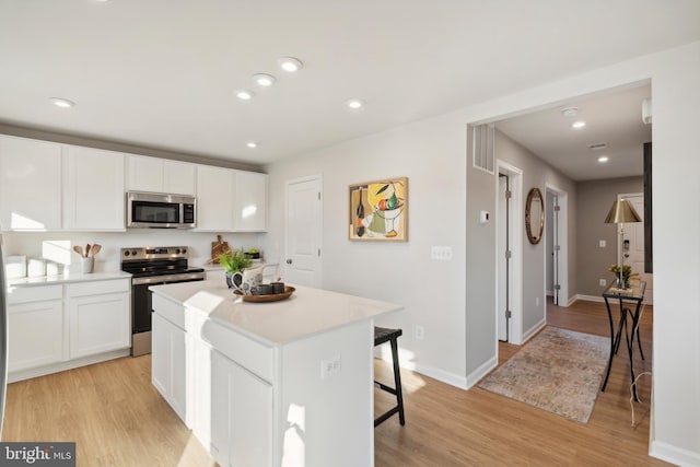 kitchen with a kitchen breakfast bar, white cabinets, appliances with stainless steel finishes, and light wood-style flooring