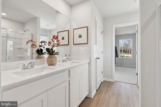 full bathroom featuring a shower stall, wood finished floors, double vanity, and a sink