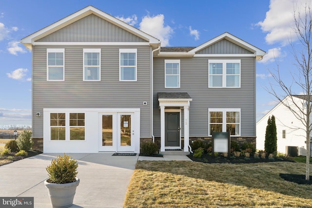 view of front facade featuring stone siding, board and batten siding, central AC unit, and a front lawn