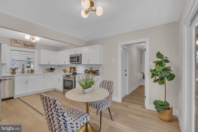 kitchen featuring light wood-style flooring, tasteful backsplash, white cabinetry, appliances with stainless steel finishes, and baseboards