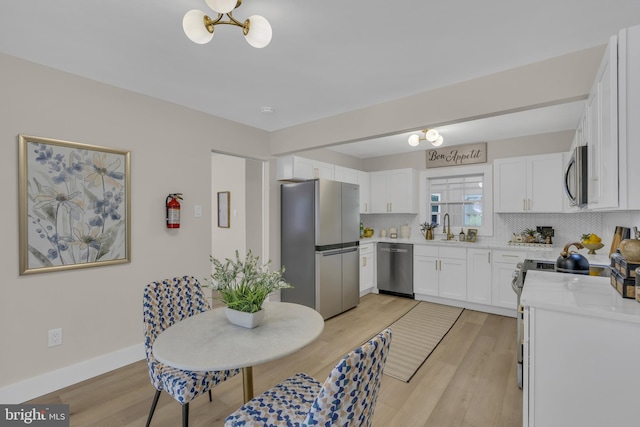 kitchen featuring tasteful backsplash, light countertops, appliances with stainless steel finishes, an inviting chandelier, and a sink