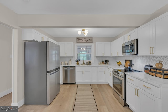 kitchen with light wood-style flooring, tasteful backsplash, white cabinetry, appliances with stainless steel finishes, and baseboards