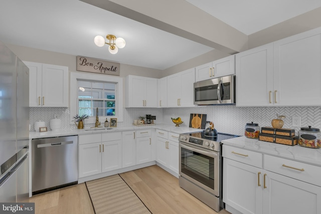 kitchen with light stone countertops, appliances with stainless steel finishes, white cabinetry, and a sink