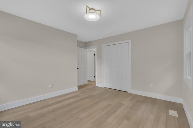 unfurnished bedroom featuring light wood-type flooring, baseboards, and a closet