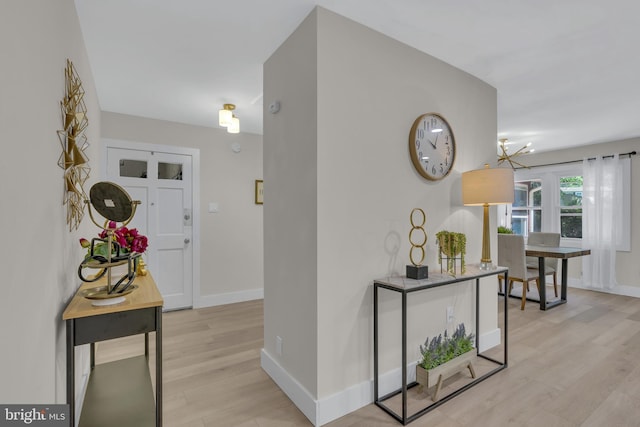 hall with a notable chandelier, light wood-style flooring, and baseboards