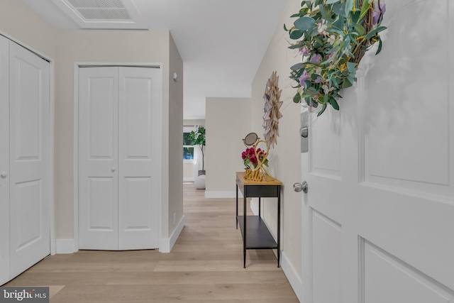 hall featuring light wood finished floors, visible vents, and baseboards