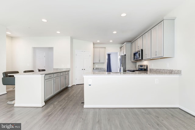 kitchen featuring light stone counters, light wood finished floors, a peninsula, recessed lighting, and stainless steel appliances