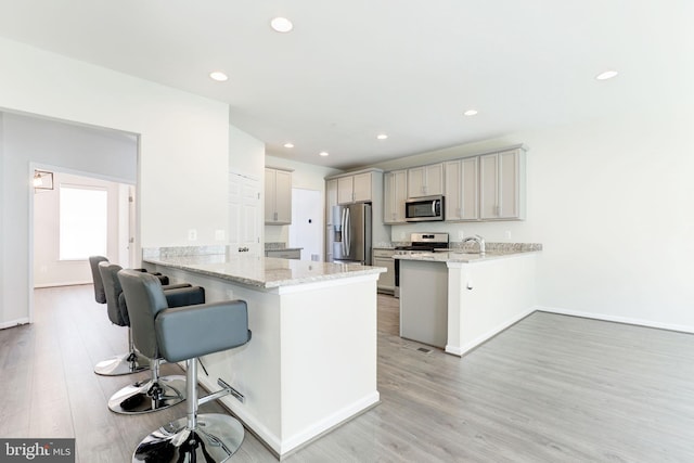 kitchen featuring a breakfast bar area, light stone counters, a peninsula, light wood-style flooring, and stainless steel appliances