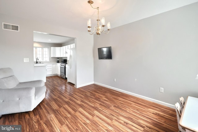 unfurnished living room featuring visible vents, dark wood-type flooring, a sink, an inviting chandelier, and baseboards