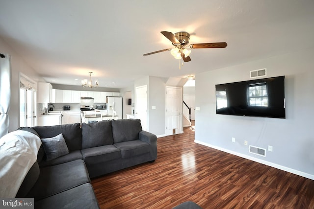 living room with dark wood finished floors, visible vents, ceiling fan with notable chandelier, and baseboards