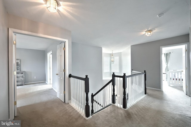 hallway featuring an upstairs landing, carpet flooring, an inviting chandelier, and baseboards