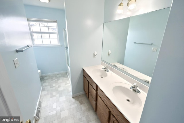 bathroom featuring double vanity, toilet, baseboards, and a sink