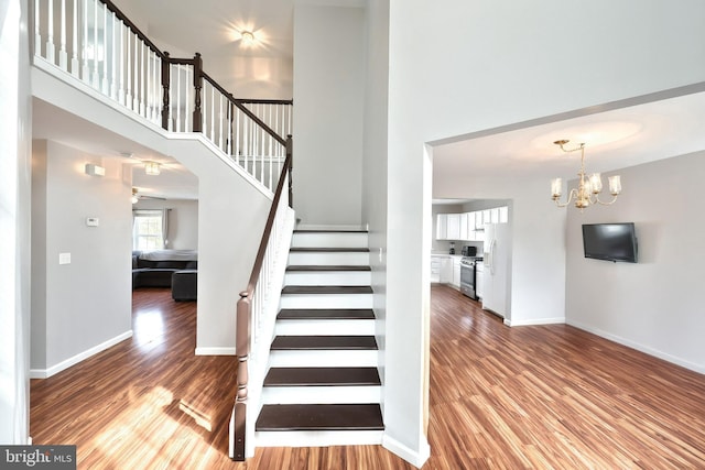 staircase featuring baseboards, wood finished floors, and a towering ceiling