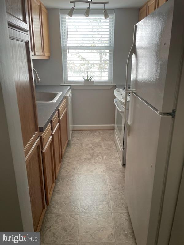 kitchen with brown cabinets, a sink, white appliances, light tile patterned floors, and baseboards