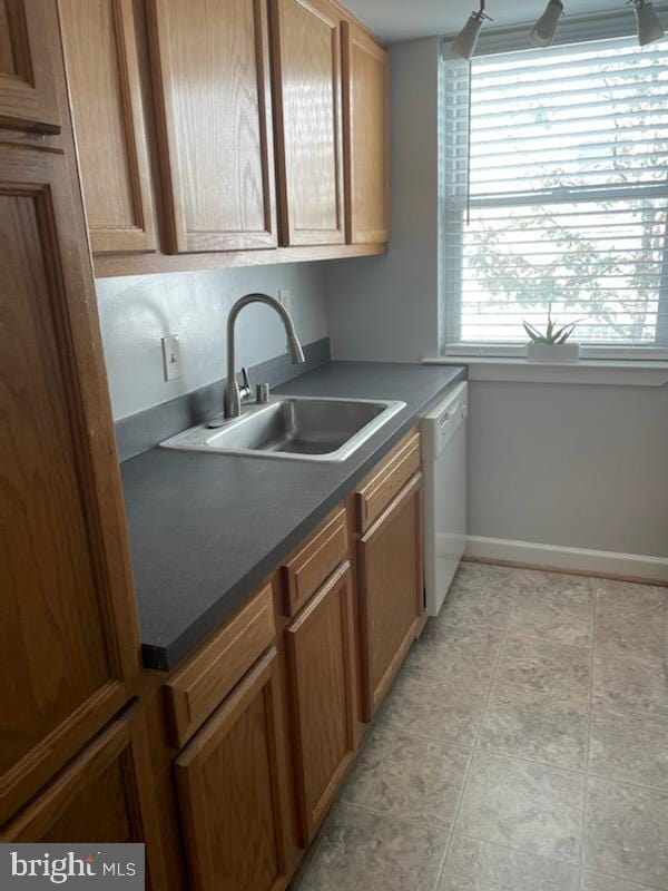 kitchen with light tile patterned floors, baseboards, a sink, dishwasher, and dark countertops