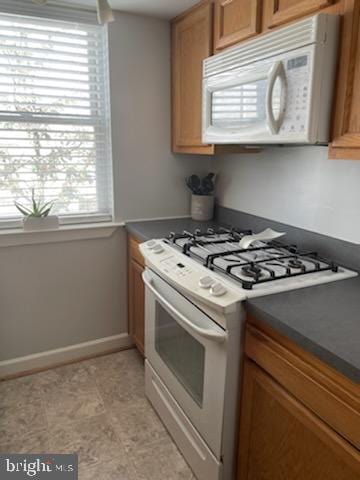 kitchen with dark countertops, brown cabinets, white appliances, and baseboards