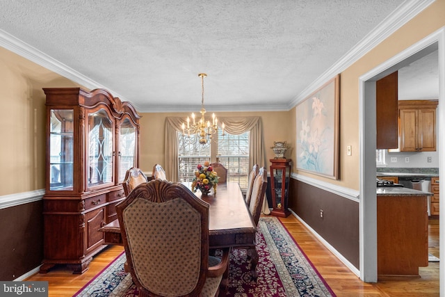 dining area with a textured ceiling, an inviting chandelier, light wood-style flooring, and ornamental molding