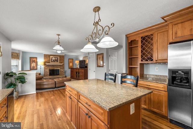 kitchen with stainless steel fridge, a kitchen island, brown cabinets, and wood finished floors