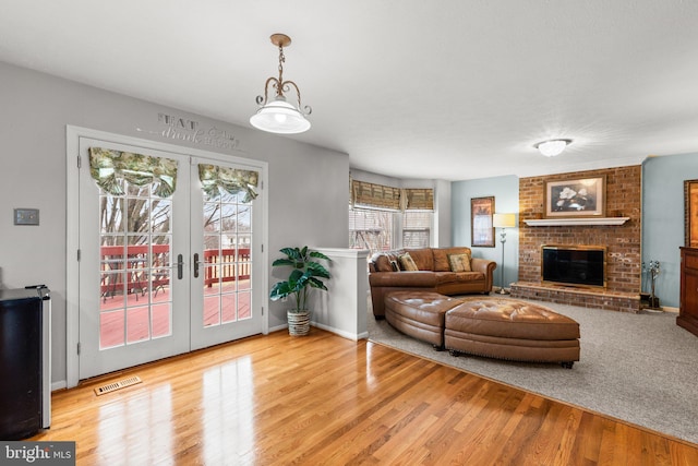 living area with visible vents, a brick fireplace, baseboards, french doors, and wood finished floors