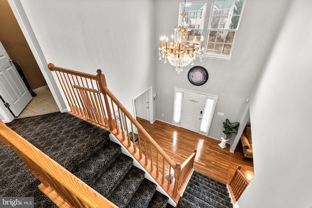 foyer entrance with baseboards, stairway, wood finished floors, a towering ceiling, and an inviting chandelier