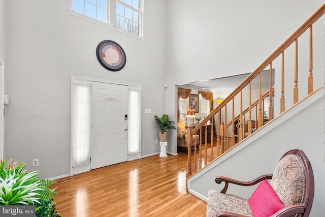 entrance foyer with visible vents, baseboards, stairway, a high ceiling, and wood finished floors