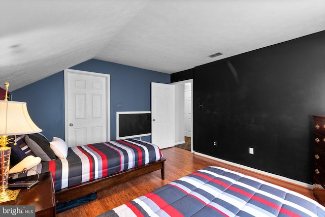 bedroom with vaulted ceiling, wood finished floors, visible vents, and baseboards