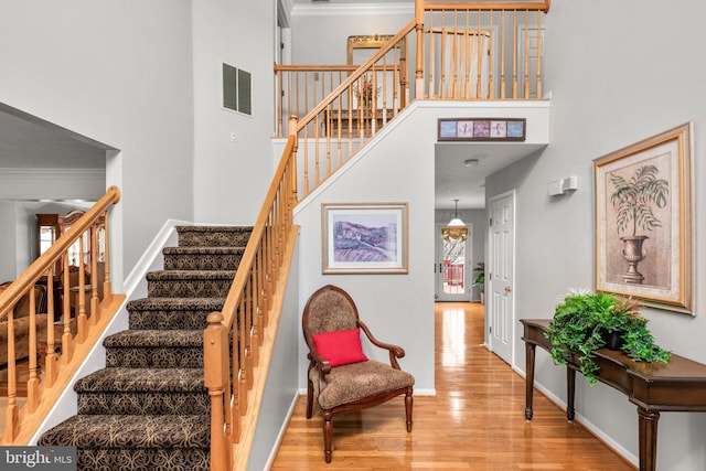 staircase with visible vents, crown molding, baseboards, a towering ceiling, and wood finished floors