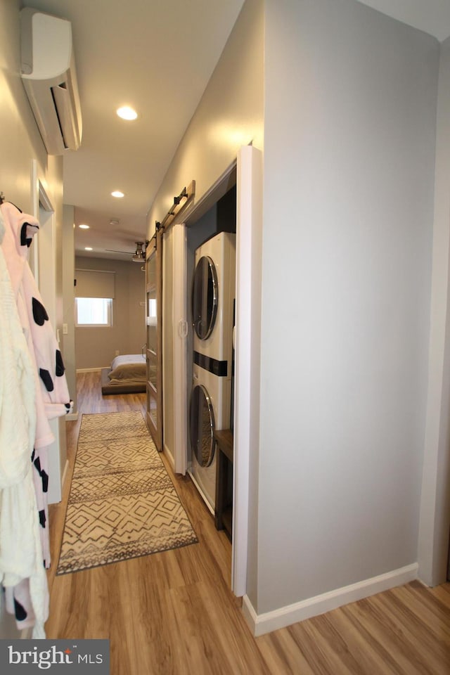 laundry area with baseboards, a wall mounted AC, stacked washing maching and dryer, laundry area, and light wood-style flooring