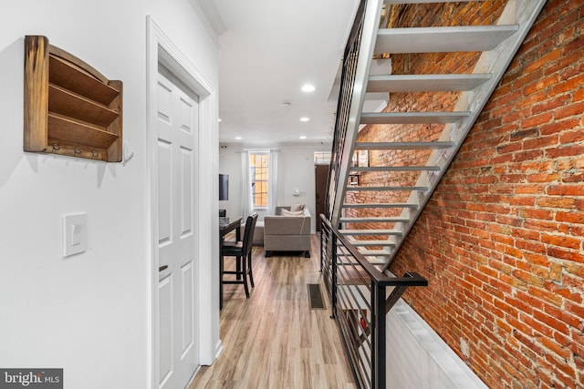 hall featuring visible vents, brick wall, stairs, light wood-type flooring, and ornamental molding