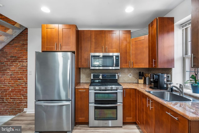 kitchen with brown cabinetry, light stone countertops, a sink, decorative backsplash, and appliances with stainless steel finishes