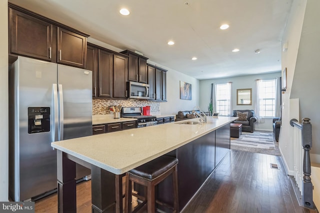 kitchen with dark brown cabinetry, a sink, appliances with stainless steel finishes, a center island with sink, and decorative backsplash