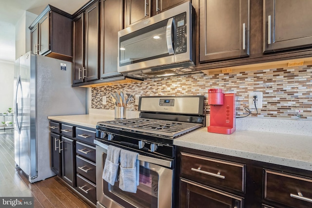 kitchen featuring light stone countertops, appliances with stainless steel finishes, dark brown cabinetry, dark wood-style floors, and backsplash