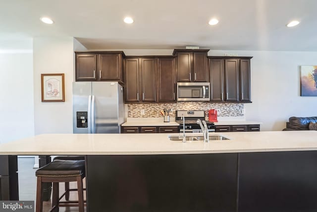 kitchen with dark brown cabinets, decorative backsplash, a sink, and stainless steel appliances