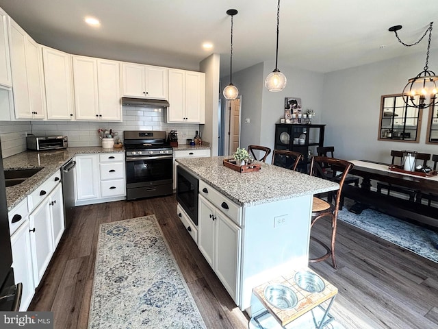 kitchen with backsplash, dark wood-type flooring, under cabinet range hood, a kitchen bar, and stainless steel appliances