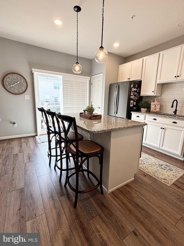 kitchen featuring light stone counters, a kitchen island, dark wood finished floors, white cabinetry, and freestanding refrigerator